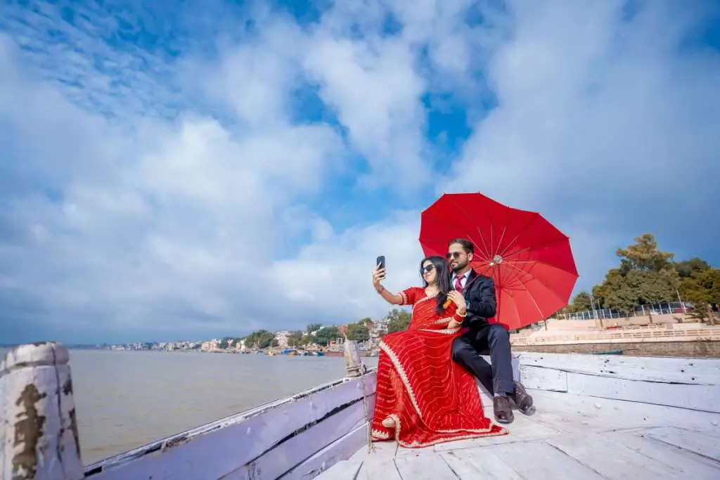 Romantic pre wedding couple taking selfie on wooden boat with red umbrella