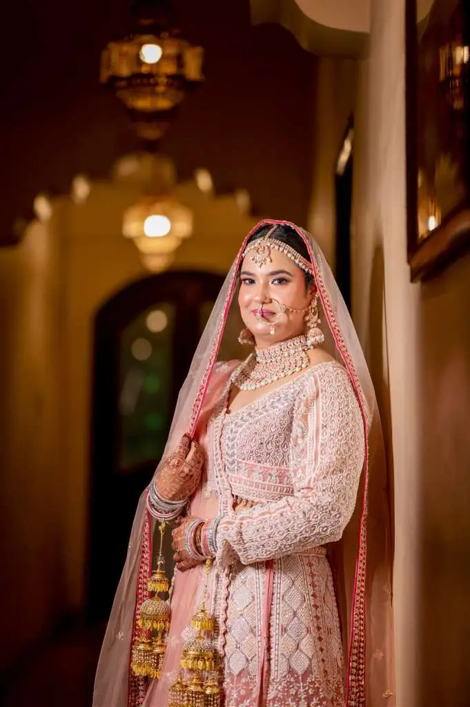 Close-up portrait of an Indian bride in pastel pink lehenga with heavy bridal jewelry and elegant soft lighting.