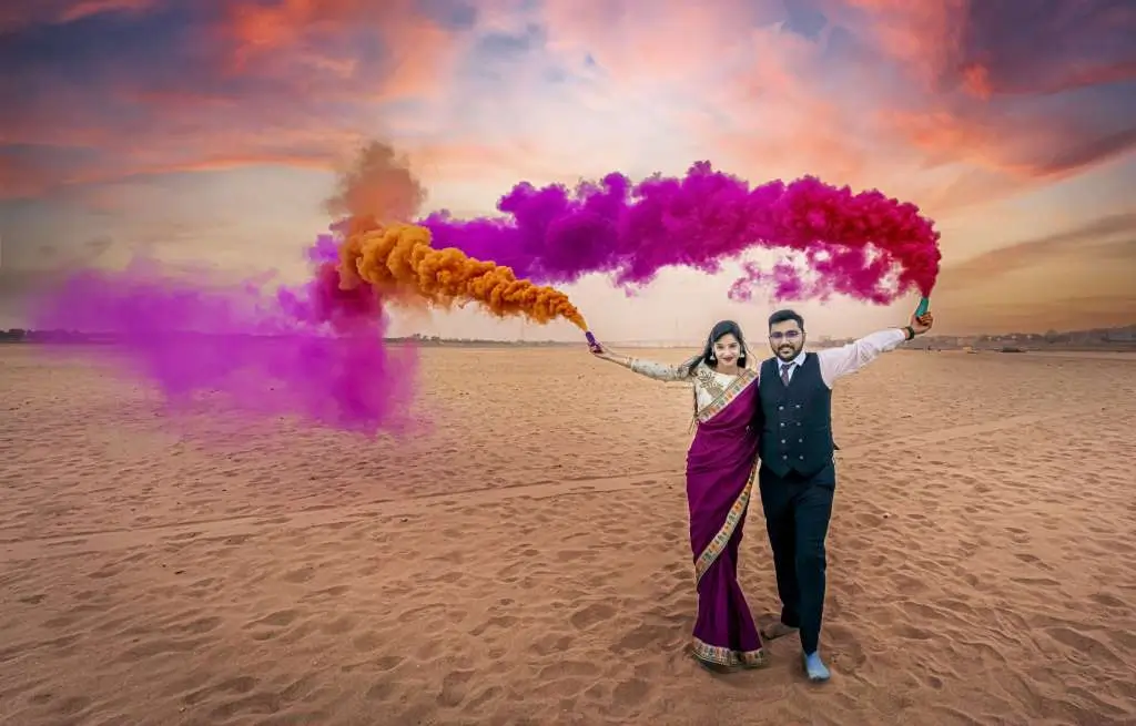 Creative pre wedding couple photoshoot with colorful smoke bombs in sandy landscape