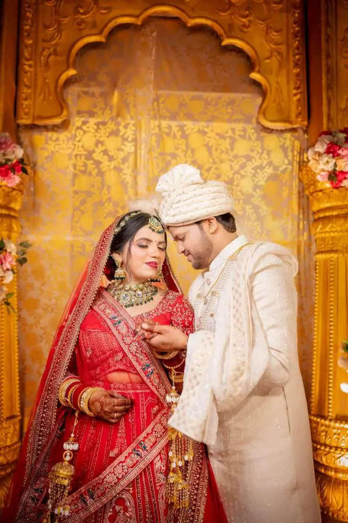 Romantic portrait of Indian bride and groom in traditional wedding attire posing together on an elegant golden wedding stage.