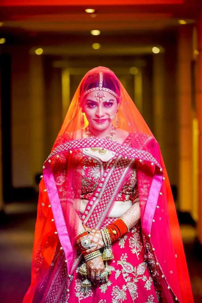 Stunning Indian bride portrait in red bridal lehenga and transparent veil with elegant wedding jewelry and cinematic lighting.
